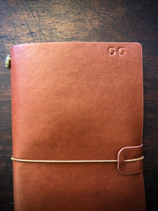 Close up image of the vegan leather journal shown in nutmeg with optional extra of embossed initials in top right cover of cover. Letters approx. 1cm in height. Journal has a matching coloured elastic band around middle to keep it closed.