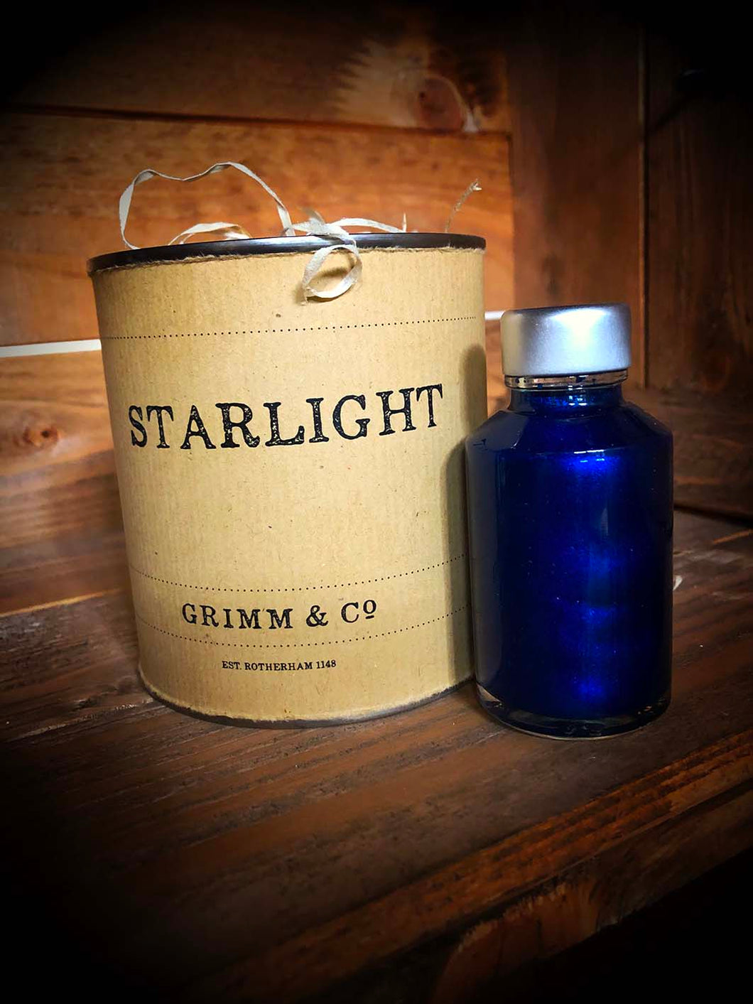 Starlight, a tin containing blue and silver shimmering ink suitable for writing and drawing. Ink bottle is shown next to the tin.
