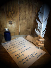 Load image into Gallery viewer, Image of a Starlight ink bottle next to a parchment page of writing done in the  blue and silver shimmering ink, with a wooden mannequin hand holding a white feather quill.