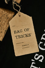 Load image into Gallery viewer, Close up of kraft paper label of black cotton tote book bag called Bag of Tricks