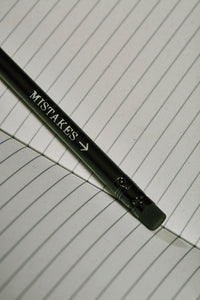 Close up details of lettering on a Word Wand, otherwise known as a black pencil with a black eraser at the top. The silver lettering in the image  reads 'Mistakes' with an arrow pointing towards the eraser.