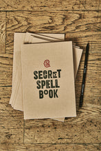 Load image into Gallery viewer, Image shows a few kraft card notebooks in a pile with the top one displaying the slogan &#39;SECRET SPELL BOOK&#39;. Notebooks are shown with a Word Wand pencil.