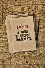 Load image into Gallery viewer, Image shows a few kraft card notebooks in a pile with the top one displaying the slogan &#39;SAUCERY: A GUIDE TO MAGICAL CONDIMENTS&#39;. Notebooks are shown with a Word Wand pencil.