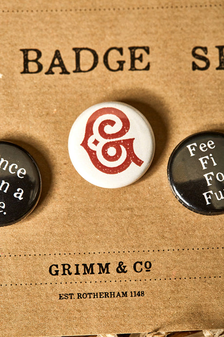 Image of a white button badge with the Grimm & Co red 'G' monogram on the front