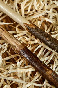 Close up image of two handmade starter wands. Wooden decorative wands with polished bark handles and stripped bare polished wooden shafts. Woods are natural shades with grain pattern. 