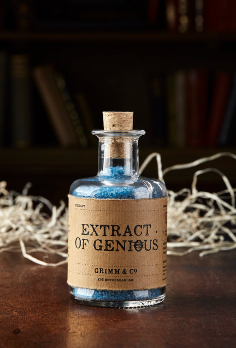 Image of Extract of Genius, otherwise known as scented, blue bath salts in a glass bottle with cork. On this label the spelling of the word Genius is deliberately misspelled to 'Genious' with the 'o' crossed out
