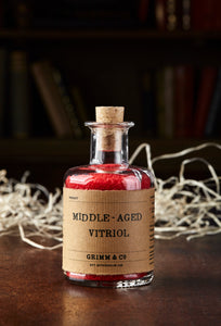Image shows a bottle of Middle Aged Vitriol, otherwise known as red, scented bath salts in a glass bottle with cork lid and a kraft paper label