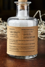 Load image into Gallery viewer, Image shows a bottle of Success Stimulant, otherwise known as white, scented bath salts in a glass bottle with cork lid and a kraft paper label. Detail of back of label showing faux ingredients and side effects for mortals.