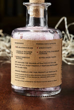Load image into Gallery viewer, Image shows the back of a bottle of Grandma&#39;s Scabs potion, a blass bottle with cork containing pale pink bath salts and dried rose petals. Bottle is wrapped with a kraft paper label, showing the faux ingredients and side effects.
