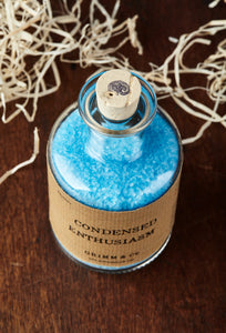 Top view image of Condensed Enthusiasm otherwise known as scented, baby blue bath salts in a glass bottle with cork