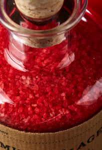 Close up image of Middle Aged Vitriol, red, scented bath salts in a glass bottle with cork.