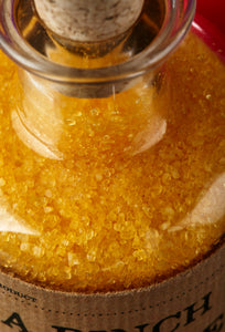 Close up image of A Pinch of Happiness otherwise known as scented, yellow bath salts in a glass bottle with cork