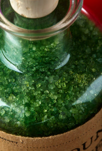 Close up image of Compound of Wicked, oherwise known as scented, green bath salts in a glass bottle with cork