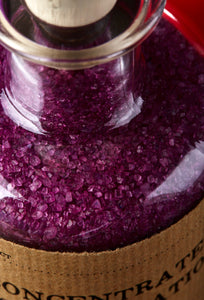 Close up image of Concentrated Concentration oherwise known as scented, purple bath salts in a glass bottle with cork