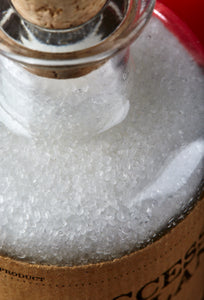 Close up image of Success Stimulant, white, scented bath salts in a glass bottle with cork.