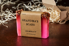 Load image into Gallery viewer, Image of Grandma&#39;s Scabs bar, otherwise known as a pink rose scented soap slice topped with dried rose petals, shown with kraft paper label