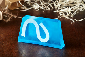 Image of Condensed Enthusiasm bar, otherwise known as an ocean scented soap slice, it is blue with a white wave shape inside the slice, shown without the kraft label