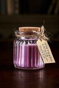 Image shows a Northern Lights Candle called Fireflies. The candle is purple coloured soy wax in a small glass pot with cork lid and is pomegranate fresh scented.
