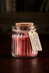 Image shows a Northern Lights Candle called Rosy Glow. The candle is pink coloured soy wax in a small glass pot with cork lid and is rose scented.