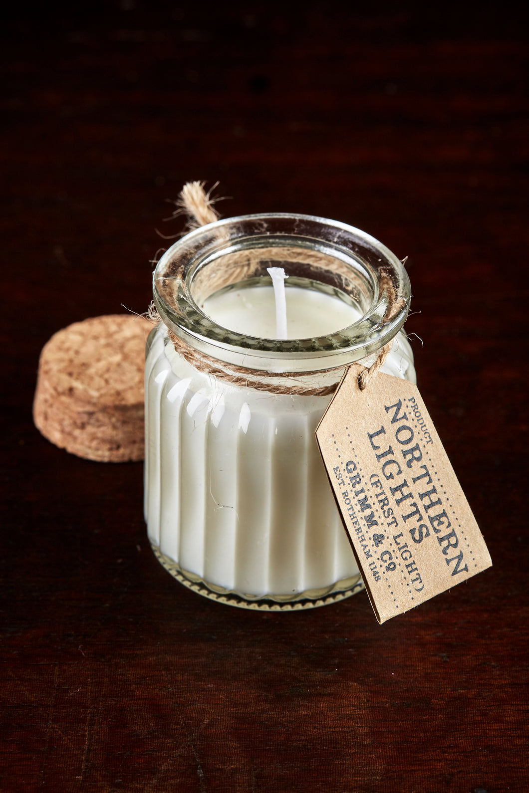 Image shows a Northern Lights Candle called First Light. The candle is white soy wax in a small glass pot with cork lid and is linen fresh scented.