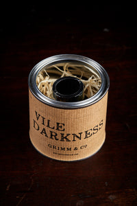 Image of a tin of Vile Darkness. A black drawing or writing ink nestled in wood wool inside the tin and wrapped with a kraft paper label. Lid in image has been removed, showing the ink bottle nestled in wood wool in the tin.