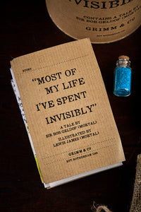 A detail image of a tin of Invisibility showing contents including a folded up illustrated story written by Sir Bob Geldof, and a tiny jar of glitter 