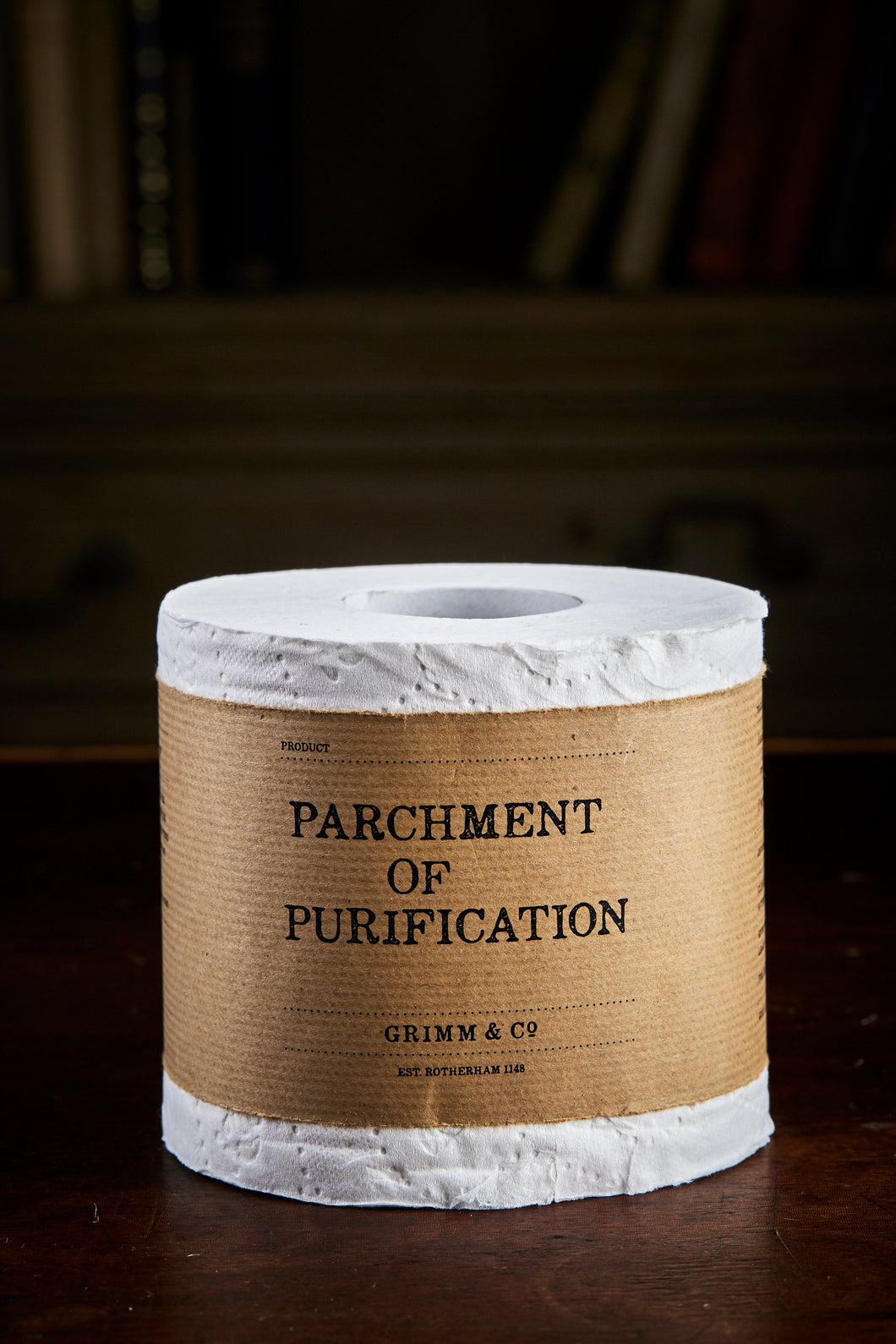 Image shows a toilet roll with a brown kraft label wrapped around the middle that reads 'Parchment of Purification'.
