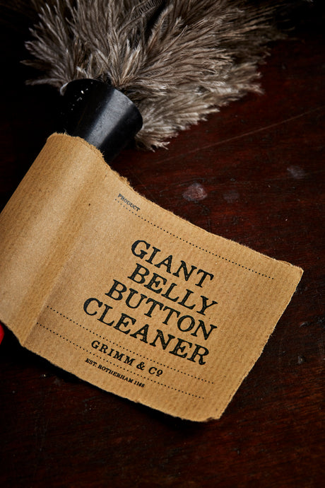 Close-up image of the Giant Belly Button Cleaner with kraft label and grey ostrich feathers attached with a black neck.