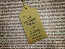 Load image into Gallery viewer, Close up of text on story excerpt scarf for Hamlet. Text is bold red cursive font on a white background. Font is size 9. Image shows kraft paper label saying &#39;An Excerpt from... Hamlet by William Shakespeare. Pair with a sense of imagination and a snazzy hat&#39;.