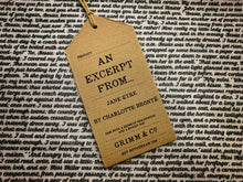 Load image into Gallery viewer, Close up of text on story excerpt scarf for Jane Eyre. Text is bold black cursive font on a white background. Font is size 9. Image shows kraft paper label saying &#39;An Excerpt from... Jane Eyre by Charlotte Bronte. Pair with a sense of imagination and a snazzy hat&#39;.
