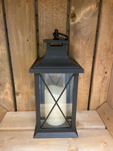 Load image into Gallery viewer, Image showing a black coloured Bright Ideas lantern with a large X lattice pattern on the windows with a battery operated candle inside and a handle on the top.