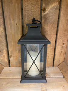 Image showing a black coloured Bright Ideas lantern with a large X lattice pattern on the windows with a battery operated candle inside and a handle on the top.