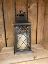 Load image into Gallery viewer, Image showing a bronze coloured Bright Ideas lantern with a small X lattice pattern on the windows with a battery operated candle inside and a handle on the top.