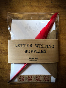 Image shows the pack of Letter Writing Supplies containing 8 sheets of cream textured paper printed with a design of potion bottles and wording, a red biro quill, 4 kraft envelops embossed with the Grimm & Co 'G' monogram and set of 4 red monogram stickers