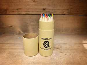 Image shows the Rainbow Word Wand Tube with the lid removed to display the coloured pencils stood inside the tube. Tube is kraft and printed with Grimm & Co and the 'G' monogram and the words Changing lives one story at a time.