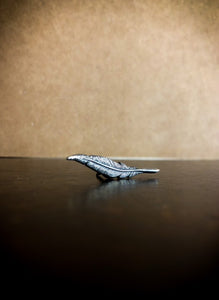 Image of a silver metal lapel pin shaped like a feather quill.