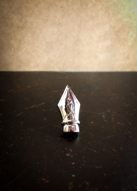 Image of a silver metal lapel pin shaped like a fountain pen nib.