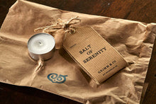 Load image into Gallery viewer, Image shows a tealight and Salt of Serenity kraft label, resting on the brown paper bag it is delivered in.