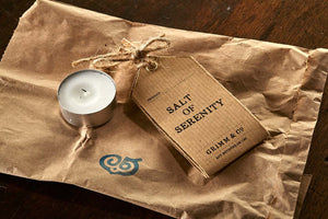 Image shows a tealight and Salt of Serenity kraft label, resting on the brown paper bag it is delivered in.