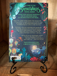 Image of the back cover of the paperback book The Strangeworlds Travel Agency: The Edge of the Ocean, written by L.D. Lapinski. Displayed on a book stand.