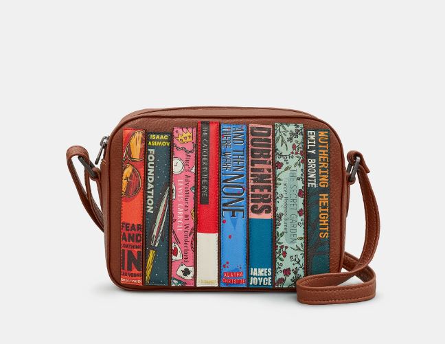 Image shows the brown vegan Yoshi camera-size bag with classic book titles appliqued to the front. Bag has an adjustable strap and zip top. Book titles include Wuthering Heights, The Secret Garden, The Catcher in the Rye and Fear and Loathing in Las Vegas.