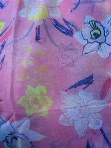 Image of the story extract scarf 'Extract from a tale in a land of wonder' with a printed pattern of yellow, pale pink and white daffodils with purple stems and leaves on a baby pink background. Image shows detail of full printed pattern.