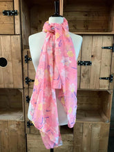 Load image into Gallery viewer, Image of the story extract scarf &#39;Extract from a tale in a land of wonder&#39; with a printed pattern of yellow, pale pink and white daffodils with purple stems and leaves on a baby pink background. Scarf displayed tied around a mannequin.
