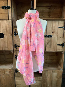 Image of the story extract scarf 'Extract from a tale in a land of wonder' with a printed pattern of yellow, pale pink and white daffodils with purple stems and leaves on a baby pink background. Scarf displayed tied around a mannequin.