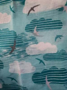 Image of the story extract scarf 'Extract from a tale on the moors' with a printed pattern of sky blue striped clouds, white clouds and swallows in grey, blue and white on a baby blue background. Image shows detail of full printed pattern.