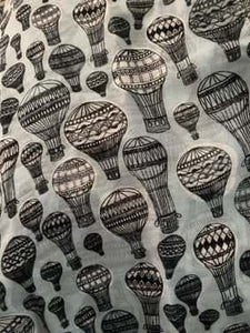Image of the story extract scarf 'Extract from a tale of travel' with a printed pattern of hot air balloons in grey and black. Image shows detail of full print pattern.