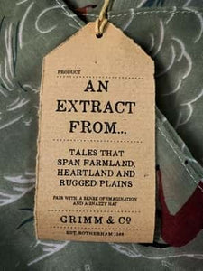 Image of the story extract scarf 'Extract from a tale on the rugged plains' with a printed pattern of linear rolling hills in white and dark teal with groups of brown and tan horses galloping amid a linear white dust cloud on a background of olive green. Kraft paper label is shown with description 'An extract from tales that spam farmland, heartland and rugged plains'.