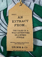 Load image into Gallery viewer, Image of the story extract scarf &#39;Extract from a tale in the jungle (green leaves)&#39; with a printed pattern of large tropical stems with white tropical and leafy flowers with leaves on a bright green background. Kraft paper label is shown with description &#39;An extract from the tales of wild adventure in a humid jungle&#39;.