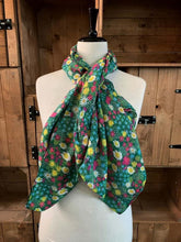 Load image into Gallery viewer, Image of the story extract scarf &#39;Extract from a tale of gardens&#39; with a printed pattern of stylized daisies, forget-me-nots, dandelions and tiny pink flowers on a grass-green background. Scarf displayed tied around a mannequin.