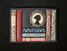 Load image into Gallery viewer, Image of the navy blue Yoshi leather card holder featuring a design of appliqued Jane Austen book spines and a printed cameo of the author inside a leather frame sat on the books. 
